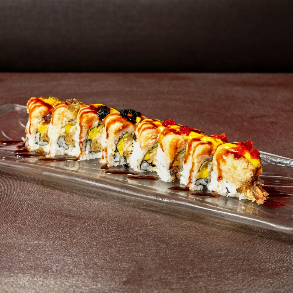 Aja Asian Cuisine's sushi roll with tempura shrimp, mango, and colorful tobiko on a glass plate.