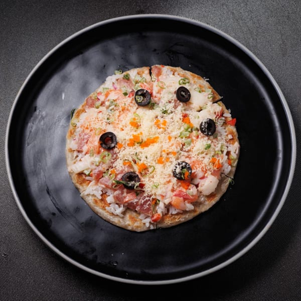 Aja Asian Cuisine's Asian pizza with rice, seafood, olives, and cheese on a black plate.