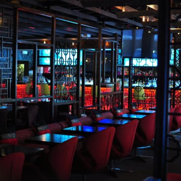Aja Asian Cuisine & Lounge's dimly lit interior with red chairs, dark tables, and glowing blue and red accents.