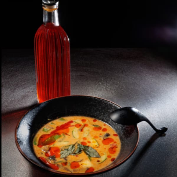 Aja Asian Cuisine's spicy red curry with vegetables and basil, next to a bottle of chili oil.