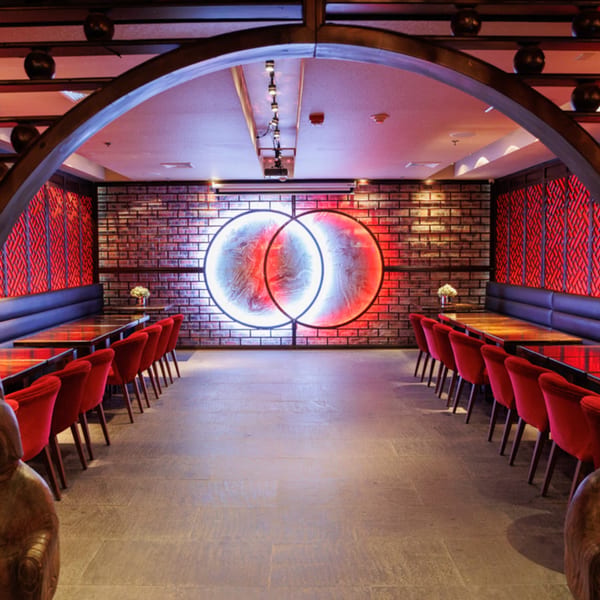 Aja Asian Cuisine & Lounge dining room with red chairs, dark tables, and a neon art piece.