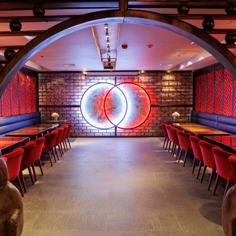 Aja Asian Cuisine & Lounge dining room with red chairs, dark tables, and a neon art piece.