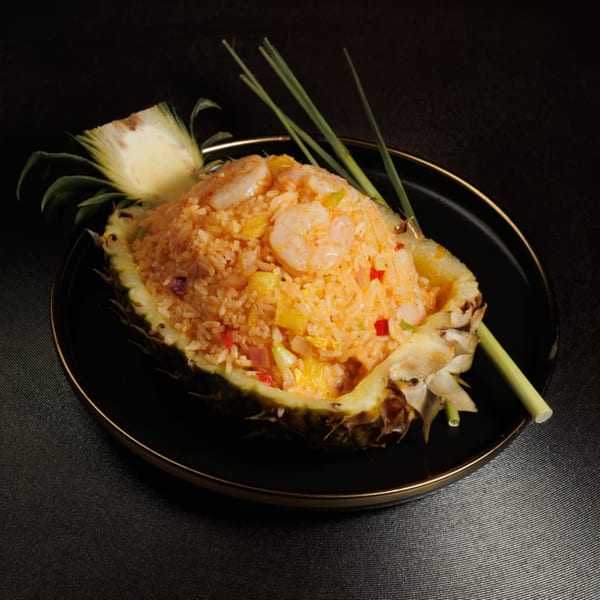 Shrimp and pineapple fried rice served in a pineapple half on a black plate with lemongrass garnish.