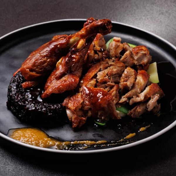 Crispy Asian duck, whole and sliced, with dark sauce and a yellow condiment on a black plate.