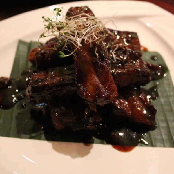 Aja Asian Cuisine's sticky ribs, glazed in a dark sauce, garnished with sprouts on a banana leaf.