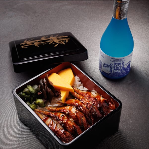 Aja Asian Cuisine's unagi donburi with tamagoyaki, pickles, and a bottle of Shirakawago sake.
