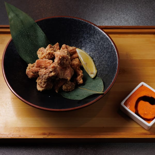 Crispy fried chicken pieces with a lemon wedge and a side of orange dipping sauce.