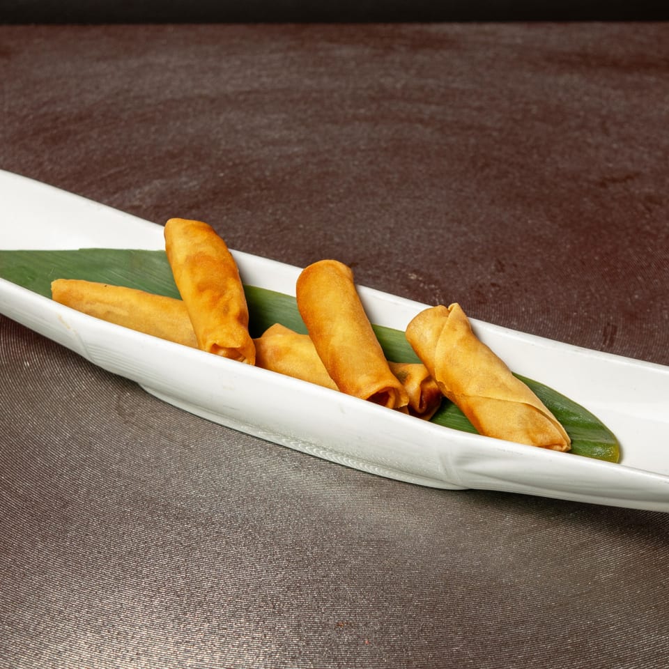 Golden-brown spring rolls on a white, leaf-lined dish, ready to be served at Aja Asian Cuisine.