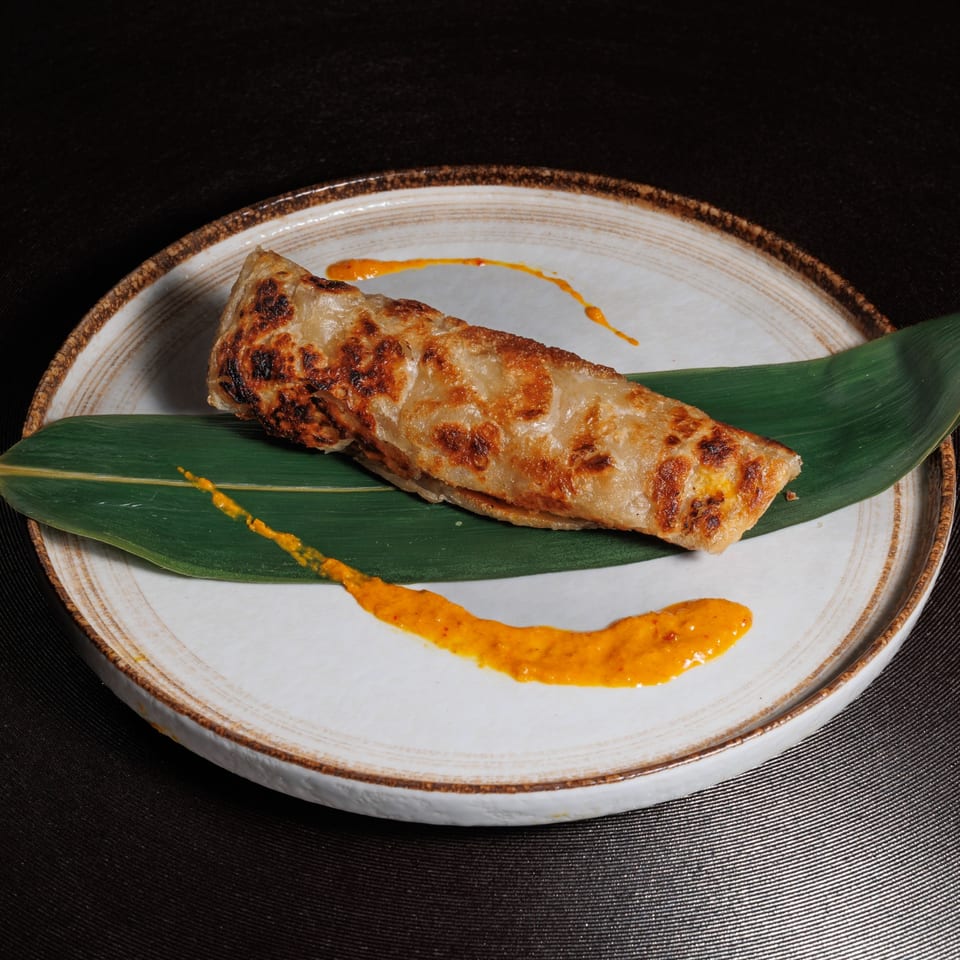 Aja Asian Cuisine's crispy Asian pancake, garnished with a green leaf and orange sauce on a white plate.