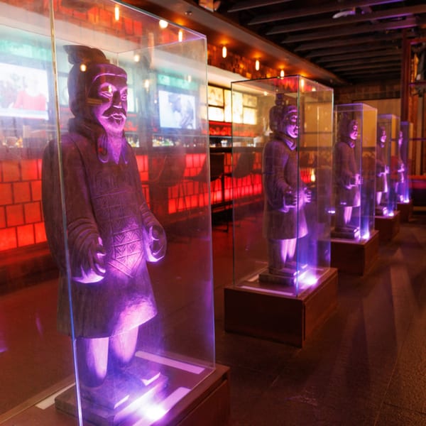 Terracotta warrior statues in glass cases with purple lighting line a dark room at Aja Asian Cuisine.