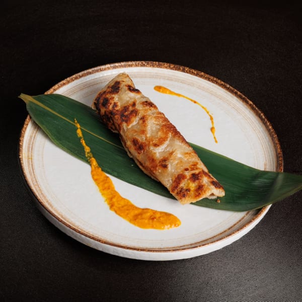 Aja Asian Cuisine's crispy roti canai with a vibrant orange curry sauce on a white plate.