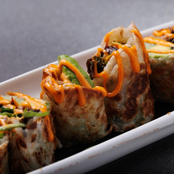 Four Asian sushi rolls with avocado and orange sauce on a white rectangular plate.
