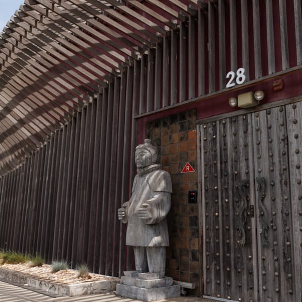 A Terracotta Warrior statue stands beside the wooden entrance of Aja Asian Cuisine & Lounge.