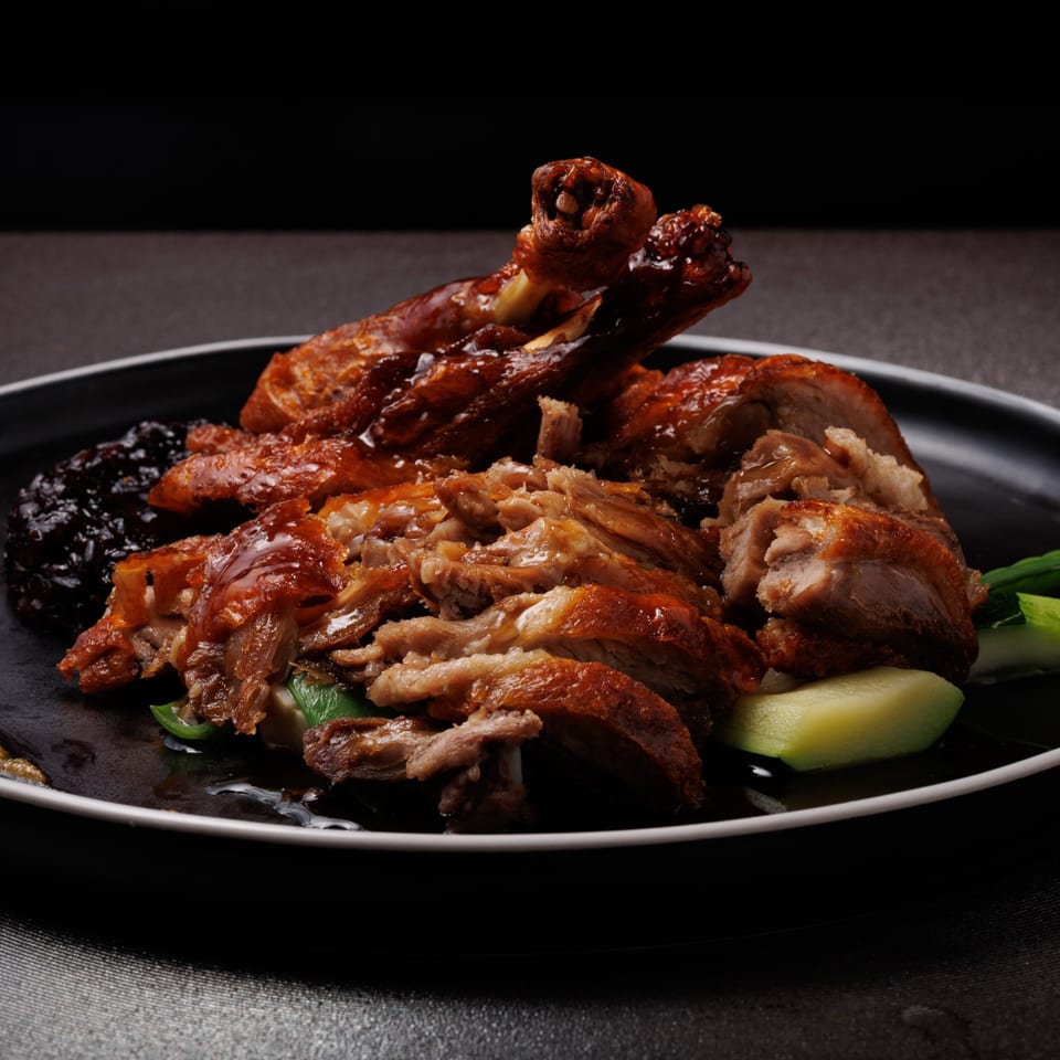 Aja Asian Cuisine's roasted duck, glistening with sauce, served with dark rice and green vegetables.