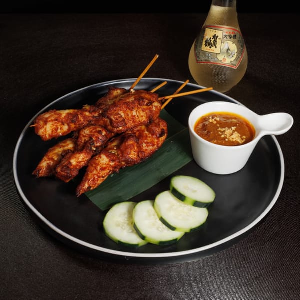 Aja Asian Cuisine's chicken satay skewers with peanut sauce, cucumber slices, and a sake bottle.