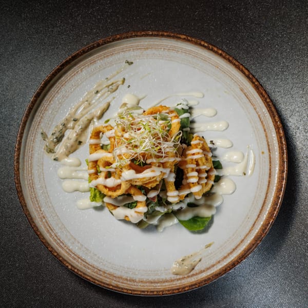 Crispy fried calamari rings with sprouts and creamy white sauce on a rustic plate.