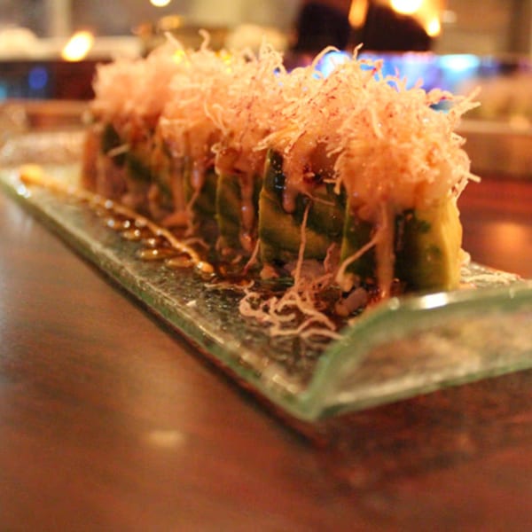 Aja Asian Cuisine & Lounge sushi roll with avocado, sauce, and crispy toppings on a glass plate.