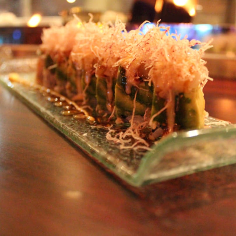 Aja Asian Cuisine & Lounge sushi roll with avocado, sauce, and crispy toppings on a glass plate.