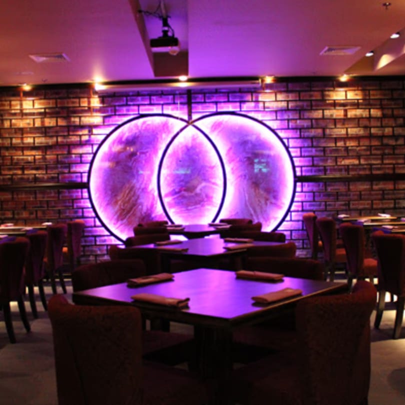 Aja Asian Cuisine & Lounge dining room with purple lighting, brick walls, and circular art.