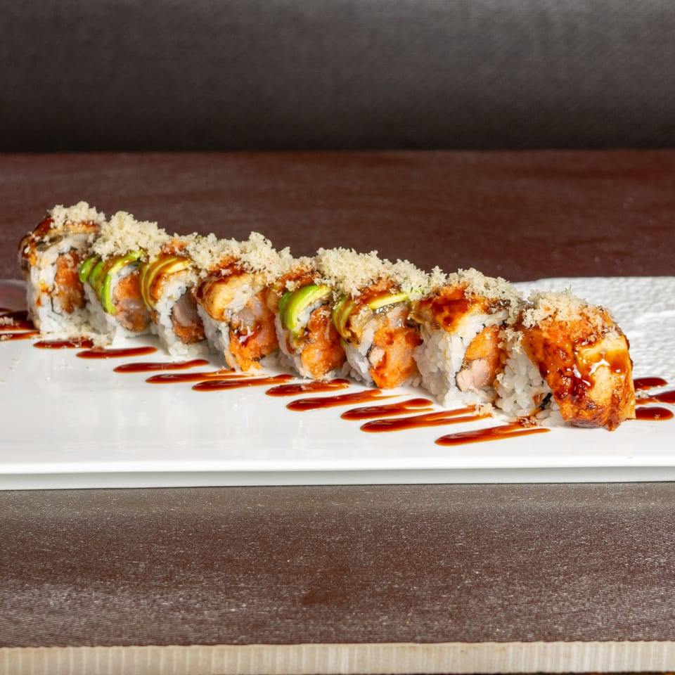 Aja Asian Cuisine's sushi roll with avocado, sauce, and crunchy topping on a white plate.